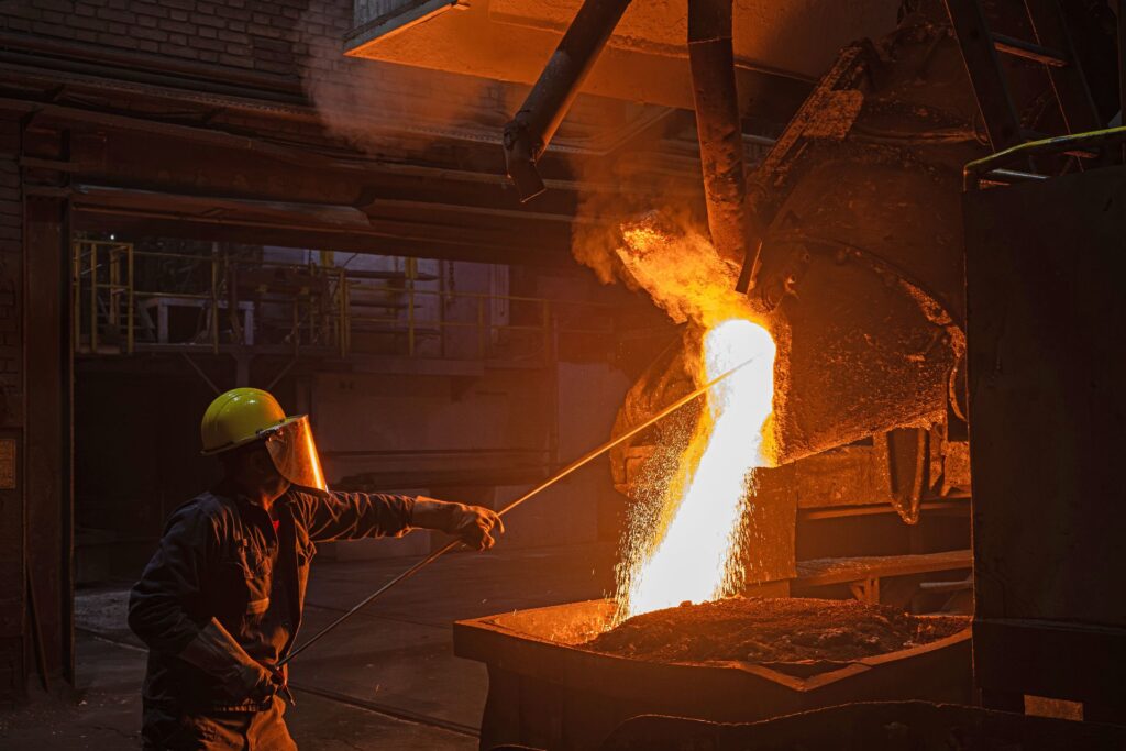 Rohstoff statt Reststoff: Graz setzt auf Kreislaufwirtschaft bei Gussrohren 3 Stahlarbeiter mit Schutzkleidung kontrolliert glühendes Flüssigmetall beim Abstich in einer Metallgießerei.