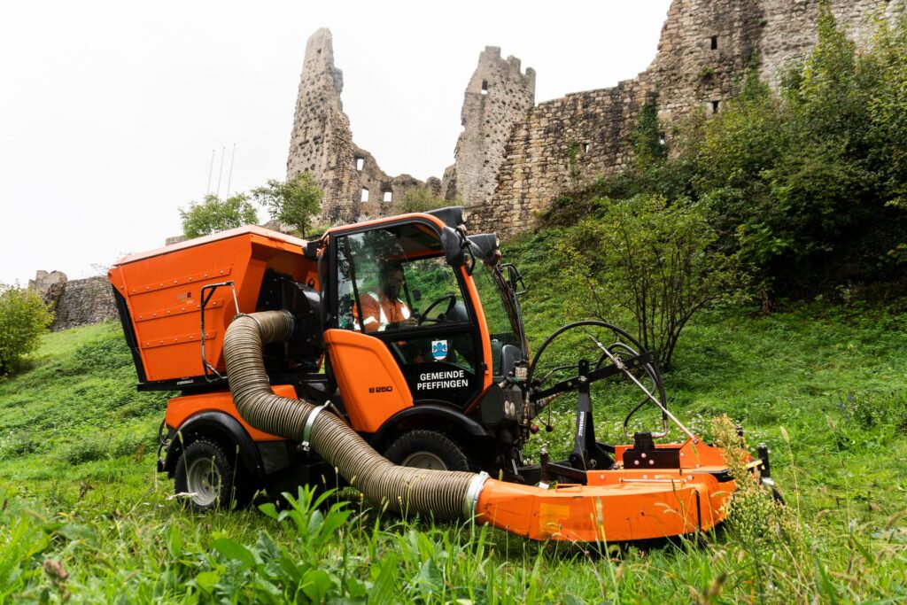 Geräteträger der Gemeinde Pfeffingen mit Mäh-Saug-Kombination vor der Burgruine Pfeffingen bei der Grünpflege.