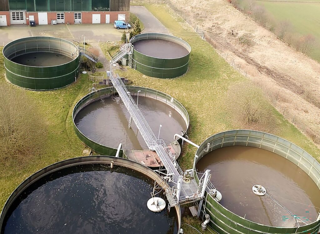 Luftbild der Kläranlage Hanerau mit fünf runden, grünen Klärbecken und Metallstegen auf einem Wiesengelände.