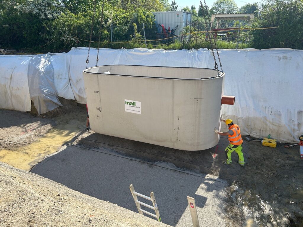 Mall Umweltsysteme Greenity Betonbehälter wird per Kran in Baugrube durch Arbeiter montiert – Mall GmbH Austria.
