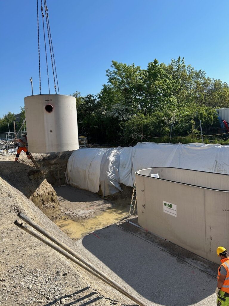 Einbau eines Greenity Betonschachts der Mall GmbH Austria mittels Kran in eine Baugrube auf einer Baustelle.
