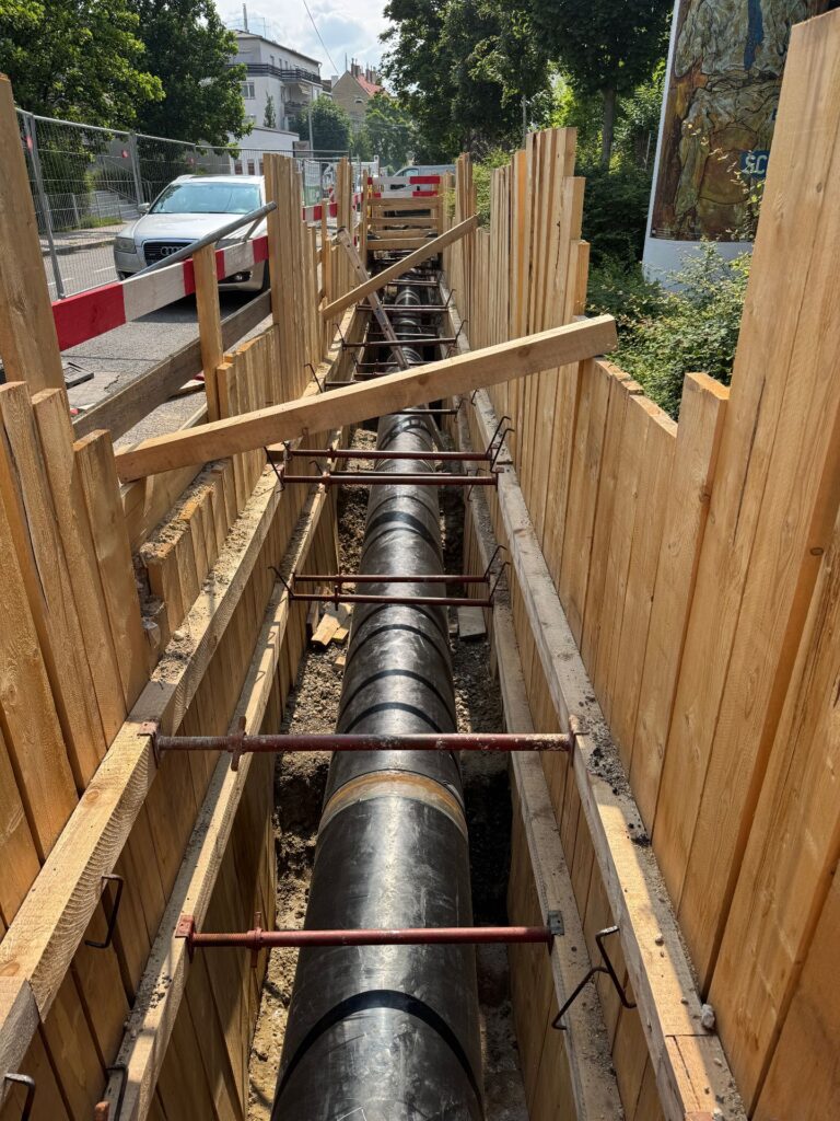 Wien stärkt das Rückgrat seiner Wasserversorgung 2 Tiefbau-Baustelle mit verlegtem Rohr in einem mit Holzbohlen gesicherten Graben an einer Straße.