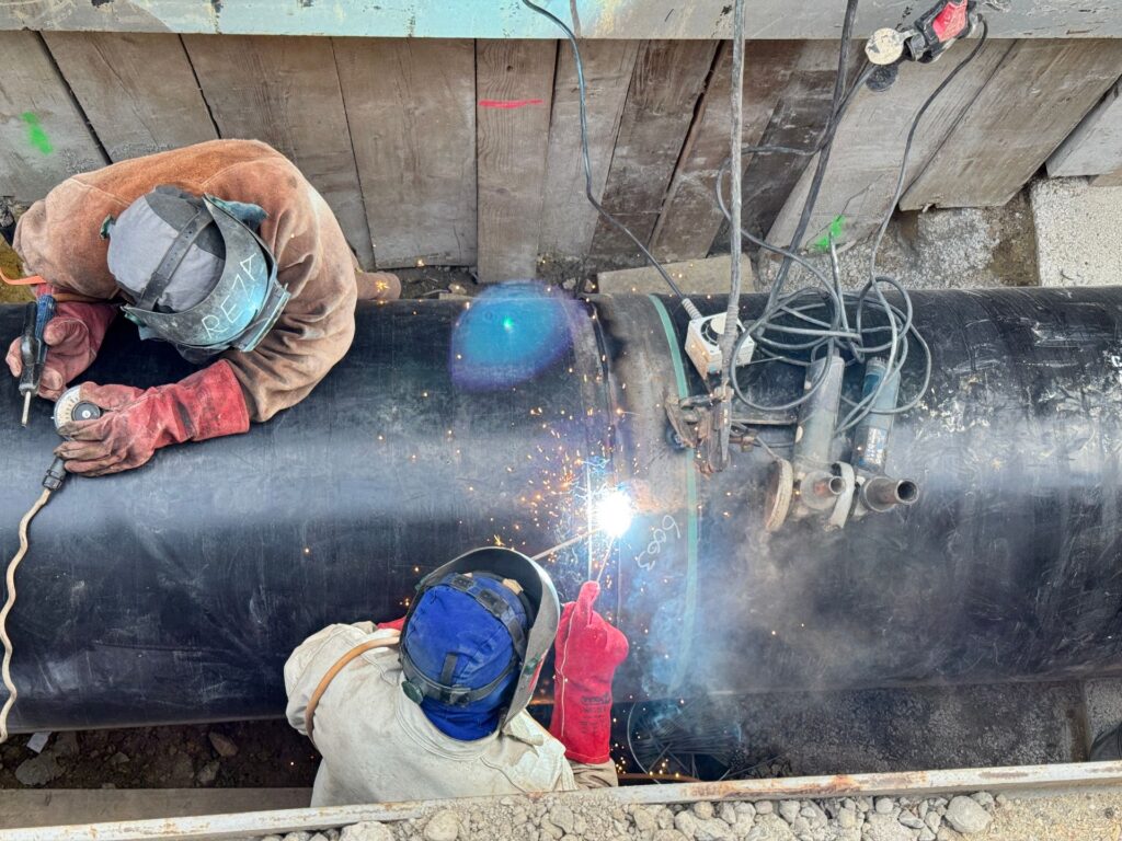 Wien stärkt das Rückgrat seiner Wasserversorgung 1 Zwei Schweißer mit Schutzhelmen arbeiten an einem großen schwarzen Stahlrohr in einer Baustellengrube mit Funkenflug.