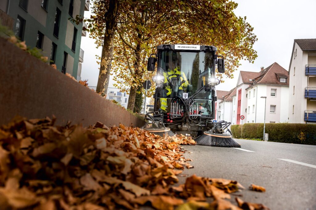 Kärcher präsentiert emissionsfreie Kommunaltechnik auf der Suisse Public 2026 3 Kärcher MC 250 electric Kehrmaschine mit 2-Besen-System bei der kommunalen Laubentsorgung auf einer herbstlichen Stadtstraße.
