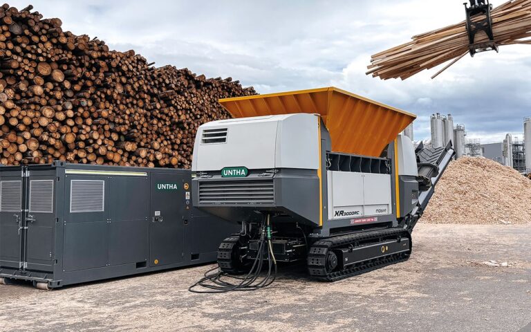 Mobile UNTHA XR3000RC Zerkleinerungsmaschine auf Kettenfahrwerk verarbeitet Altholz vor großem Baumstamm-Stapel für IFAT 2026.