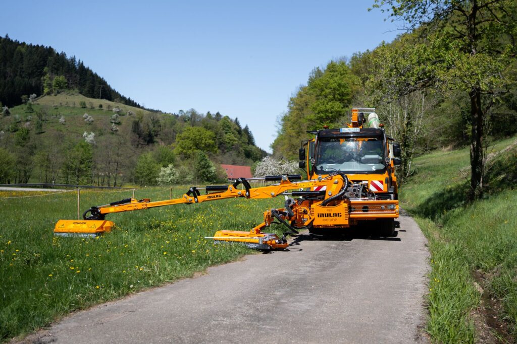 Mulag FBX Prototyp und MHU 900 Mähgerät an Unimog in Frontansicht mit maximaler Reichweite auf einer Wiese.