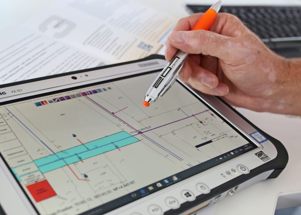 Hand mit Eingabestift bedient eine CAD-Planungssoftware auf einem robusten Tablet für die professionelle Vermessung.