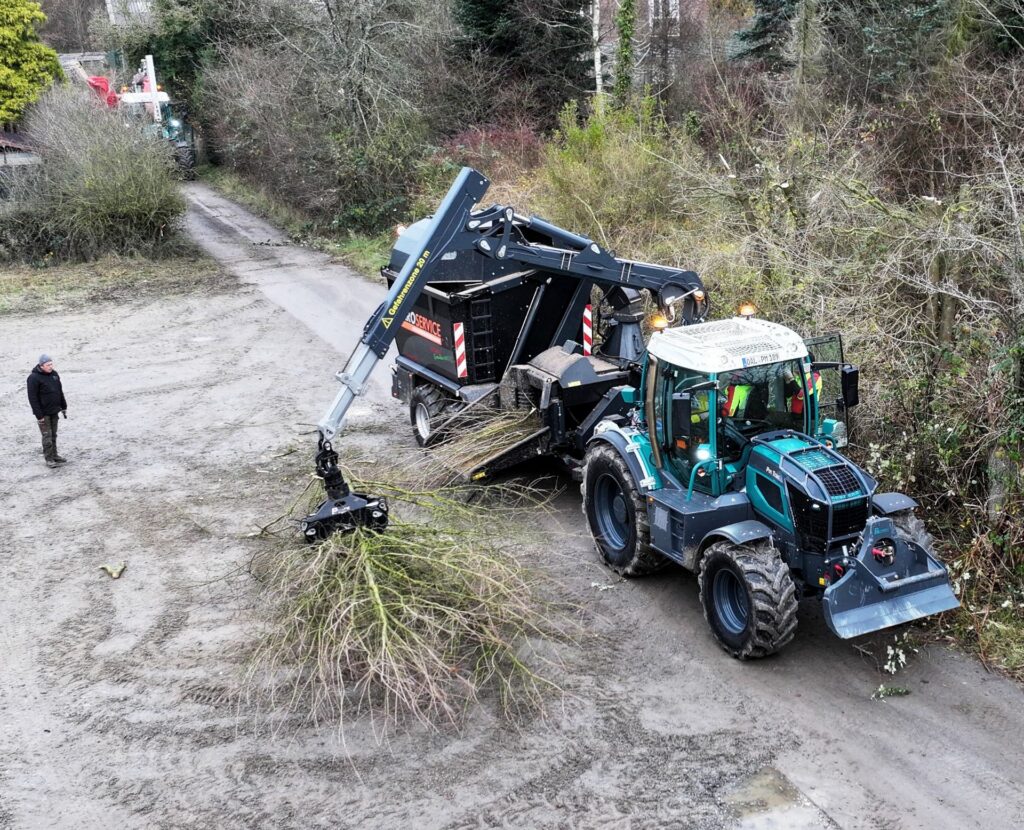 Pfanzelt Pm Trac Systemschlepper mit Holzhäcksler greift Äste am Waldrand; Forstarbeit mit Kranarm und Anhänger.