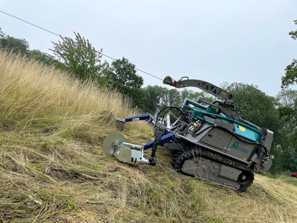Ferngesteuerte Pfanzelt Raupe mit Forstmulcher im Einsatz an einem steilen Grashang zur Landschaftspflege.